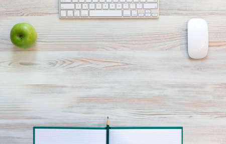 Working desk with green apple View from above on light beige wooden working desk with green apple, large notepad, computer keyboard and mouse, green pencilの写真素材