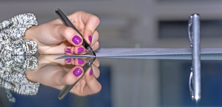 Woman hands working on paper document on glass office table making strong reflection with fountain pen stylish nail make-up soft smothered background cool tonesの写真素材