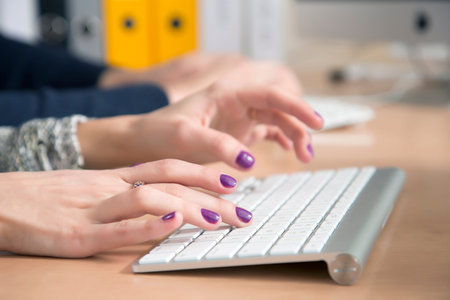 Female fingers typing on keyboard Office desk with keyboard and some other office supplies, female palms on the foreground, male hands on the backgroundの写真素材