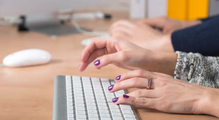 Female fingers typing on keyboard Office desk with keyboard and some other office supplies, female palms on the foreground, male hands on the backgroundの写真素材