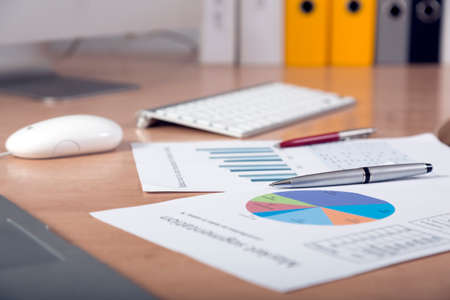 Dropped work Side view of working place with printed colored charts pens and laptop on foreground cropped big screen and office folders on the backgroundの写真素材