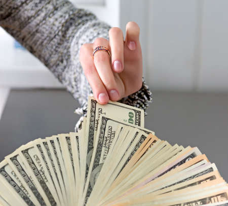 Female hand pulls out single cash note from the large stack of notes held by male hand. Caucasian people, grey wooden desk on the backgroundの写真素材