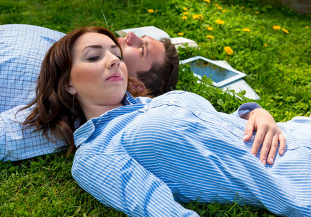 Cute young man and woman tired with work and napping on green park grass laptop tablet PC book dropped around bodiesの写真素材