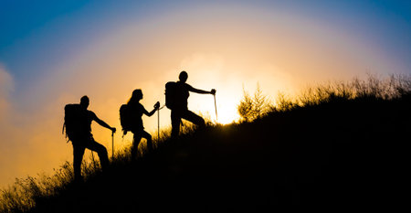 Climbers on grassy hill Family three people silhouette walking up steep grassy hill majestic sunrise and blue sky backgroundの写真素材