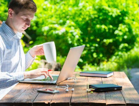 Businessman working on laptop with serious inspired face on green terrace of suburban cottage at brown natural timber wood desk backlight sun back light backgroundの写真素材