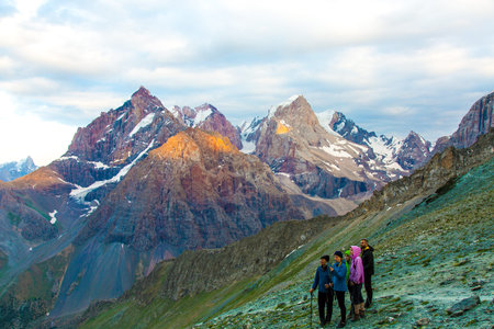 Large group of men staying on grassy trail looking side mountain peaks rocky ridge cloudy sky...