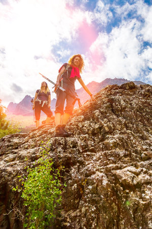 People walking on top of stone rock with trekking poles and backpacks silhouettes on clouds and sky background mountain landscape young womenの写真素材