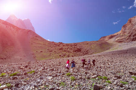 Hikers Walking Across Rocky Mountain Terrain with Blue Sky and Shining Sun on Backgroundの写真素材