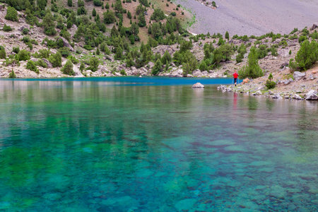 Hiker Walking on Footpath beside Shore Azure Mountain Lake Transparent Water Bottom Stones Well Visibleの写真素材