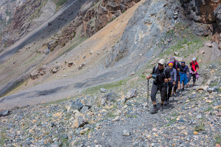 Hiker Team Scramble Up on Rocky Trail with Severe Colored Steep on Background