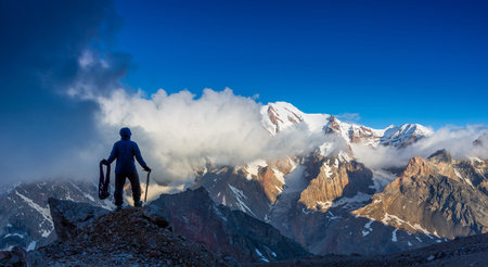 Silhouette Man Staying on Top of Rock Cliff Holding Climbing Gear Stormy Clouds and Peaks...