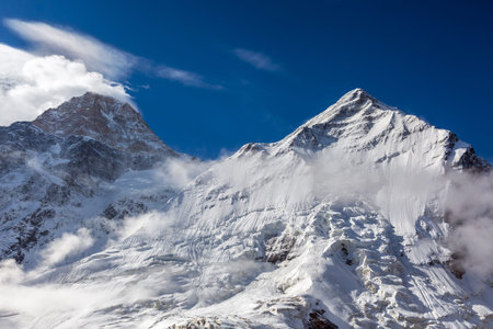 Majestic View of High Altitude Snowbound Mountain Peaks with Glaciers Rocks Snow Clouds and Blue Sky