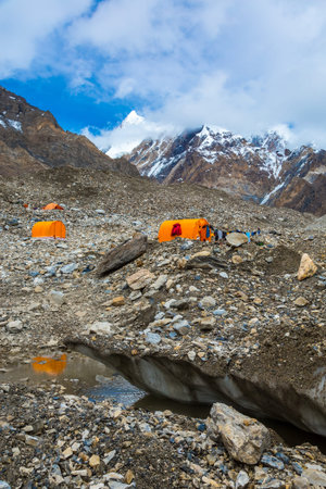 Mountain Expedition Camp on Glacier Moraine with Large Ice Crevasse and Melting Lake Foreground...
