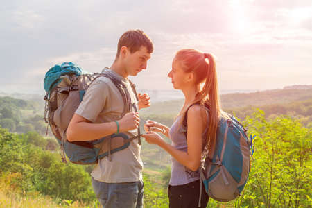 Girlfriend and Boyfriend Teenagers Couple with Backpacks on Green Forest Background Staying Talking Smiling rising Sun on Backgroundの写真素材