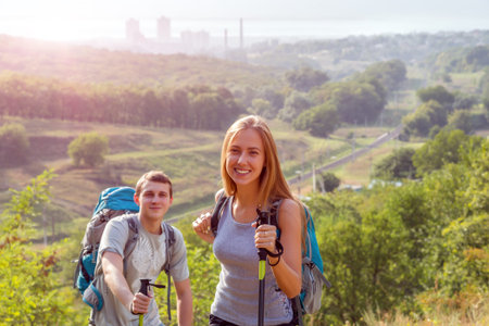 Young Man and Woman Traveling Outdoor Expressing Fun and Pleasure with Backpacks Walking Poles...