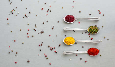 Image of Grey Metal Spoons with Selection Aromatic Seasonings Classic Grey Wooden Background balls of white red black pepper and pieces of cloves dropped aroundの写真素材