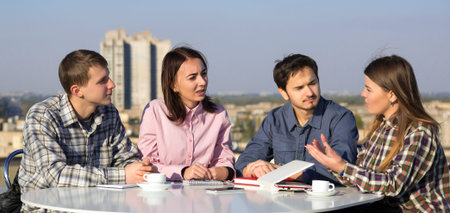 Group of Young Casual Dressed People on Informal Business Meeting at White Rounded Table Roof Top...