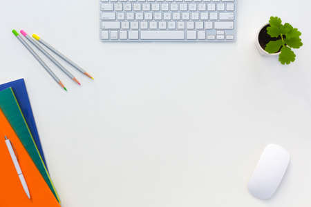 Creative Office White Table with Color Orange Green Blue Magazines and Pencils Computer Keyboard Mouse and Green Flower Top Viewの写真素材