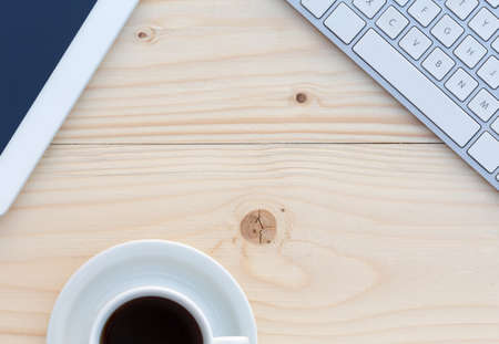 Top View of Wood Table with Computer Keyboard Tablet PC and White Coffee Cup on fresh batten textureの写真素材