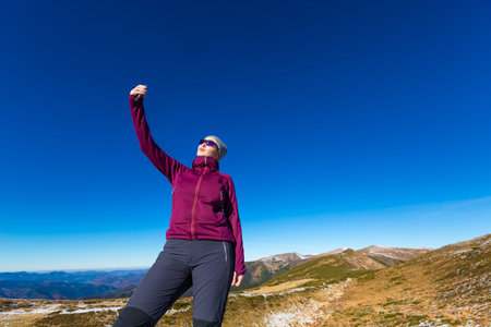Elegant Female Hiker Making self portrait Selfie on mobile Phone Mountains View blue Sky Daylightの写真素材