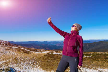 Cute Woman in sporty Clothing making self portrait selfie on mobile Phone Mountains View and Sun Shiningの写真素材