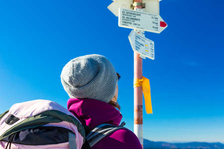 Hiker with Backpack Staying and Looking on Trail Sign sporty Clothing blue Skyの写真素材