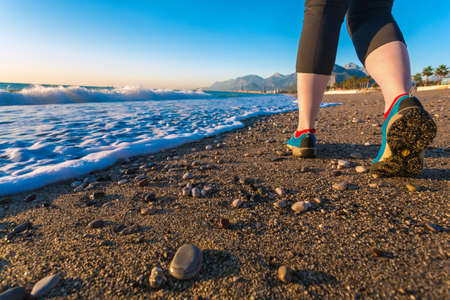 Young Woman walking on Sand Beach along Sea Surf at Morning bright blue Shoes and waves Close Upの写真素材