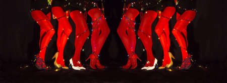 Legs of female cabaret dancers with christmas lights tied around body in red leggings and high heels shoes on dark backgroundの写真素材