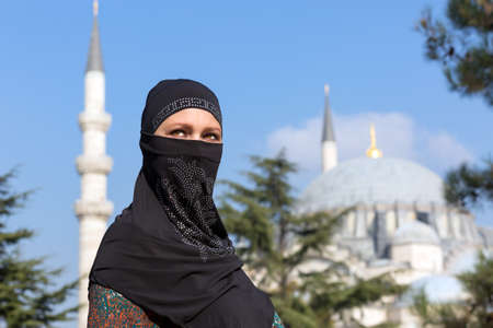 Portrait of beautiful Arabian Woman in traditional Muslim Clothing Middle East Urban landscape with Mosque and Minarets on Backgroundの写真素材