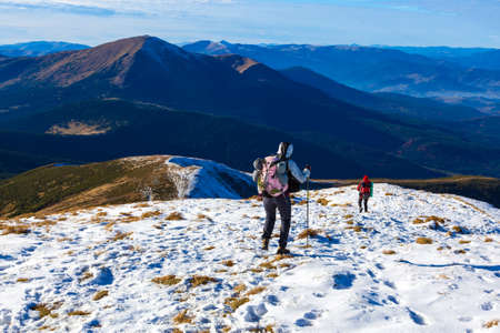 Winter Mountain Range View and Group of Trekkers Walking on Snow Trail Carrying Backpacks and Using Hiking Poles Clear Blue Skyの写真素材