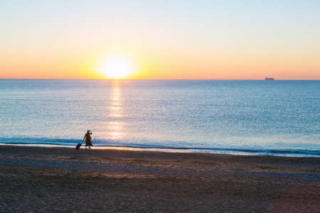 Around the World Exotic Vacation Concept Silhouette of Female pulling Travel Suitcase along Ocean Beach Luminous Sunrise on Backgroundの写真素材