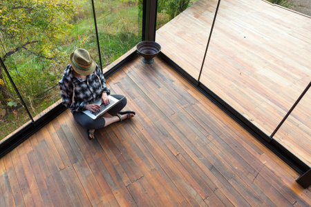 Casual dressed person sitting on Wood Floor of Rural Bungalow and working on Laptop