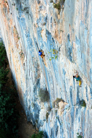 High vertical unusual orange and blue colors rocky Wall and two male Climbers moving upの写真素材