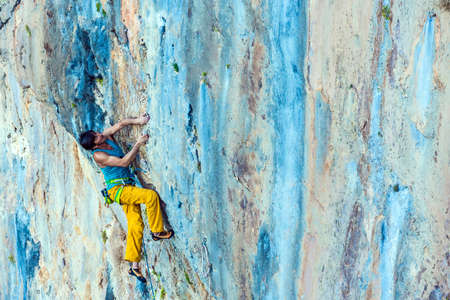 Side View of Male Climber hanging on vertical Rock with unusual shape and orange blue colorsの写真素材