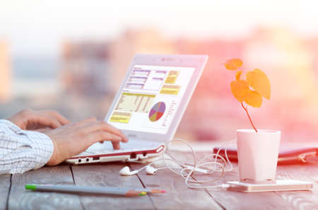 Workplace at Outdoor Patio and Hands of Person smart casual clothing typing on Laptop electronic Gadgets and color Pencils dropped around Focus on plant leavesの写真素材