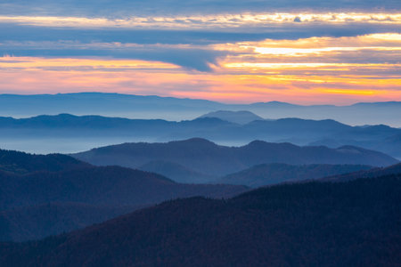 Mountains and Hills panoramic View with many stacked foggy and smoky Ranges and Ridges Valleys covered by Clouds evening Sky with bright Colors of Sunsetの写真素材
