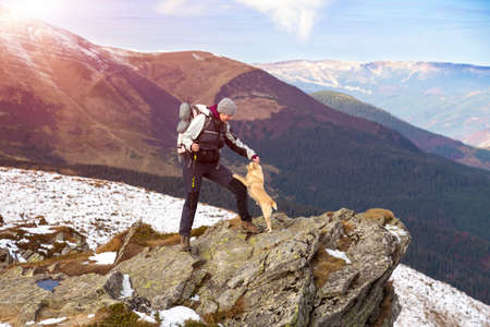 Female Hiker with Backpack and walking Poles staying at rocky Mountains Cliff and playing with accompanying Dog view with green Hills and Sky on Backgroundの写真素材