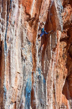 Female Climber ascending natural High Rock making elegant Move Summer style sportive Clothing High Contrast red and blue Stone Textureの写真素材