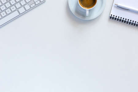Simple sparse morning Office Composition with clean White Desk and cropped Computer Keyboard Notepad Pen and Cup of Espressoの写真素材