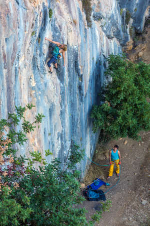 Two Climbers work in pair Female leads Male belays and watch on vertical rocky Wallの写真素材