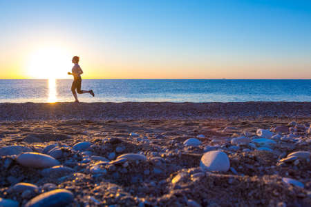 Silhouette of Person Jogging along Ocean Beach at Sunrise orange and blue tones の写真素材