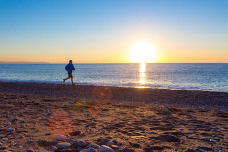 Silhouette of Person Jogging along Ocean Beach at Sunrise orange and blue tones の写真素材