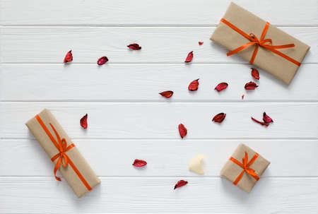 Valentine Day Concept lovely wrapped beige Color Paper and tied with red Ribbon Gift Boxes of different Shape on white Wood Background flat Lay top View Flower Petals randomly dropped with copy space.の写真素材