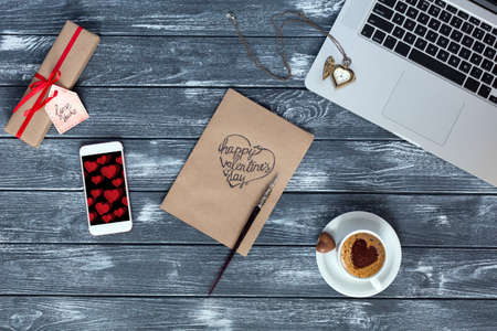 Cozy working Place top View on Valentines Day with Business Gadgets Computer and Telephone Coffee Mug handwritten Postcard and wrapped Gift Flat Lay on dark Wood Backgroundの写真素材