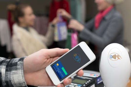 Man completing mobile Payment at Store Cashiers Desk with Terminalの写真素材