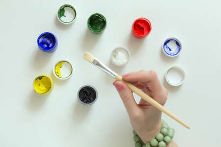 Hand of Artist holding Brush and color Paints on white Tableの写真素材