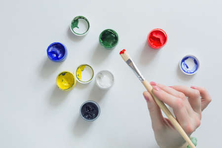Hand of Artist holding Brush and color Paints on white Tableの写真素材