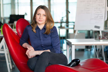 Charismatic Business Person sitting in red Chair at modern Officeの写真素材