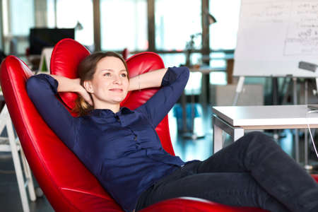 Business Person relaxing in red Chair at modern creative Officeの写真素材