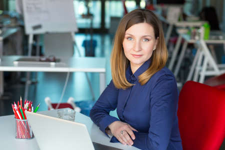 Smiling Business Lady in casual clothing sitting at Office Tableの写真素材